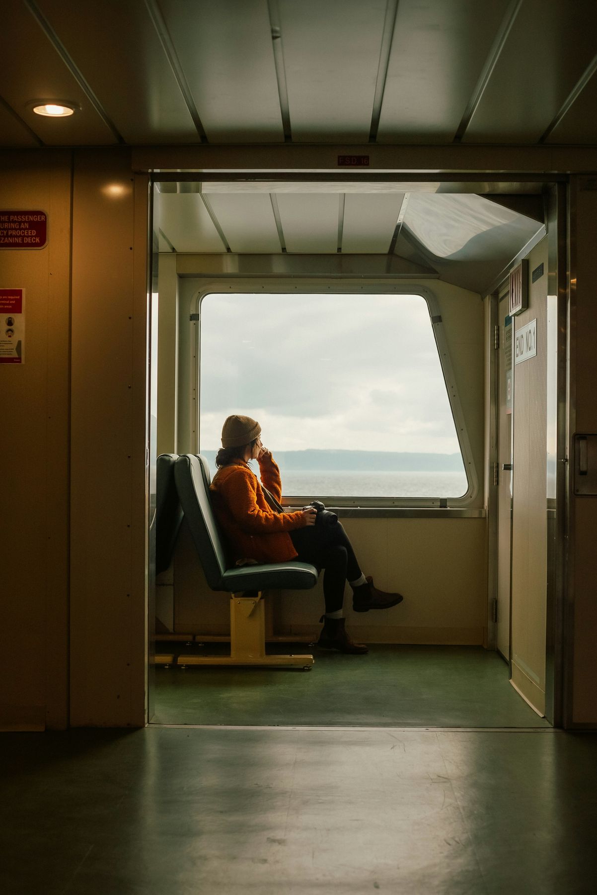 A traveler seated by a ferry window overlooking the sea